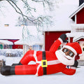 Black Santa inflatable in sunglasses lounging on his side in a snowy yard