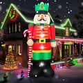 Giant nutcracker inflatable in a red coat and green crown holding a candy cane at night