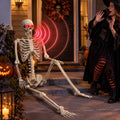 Life-size skeleton with glowing red eyes sitting on a porch step as a woman in a witch costume steps back
