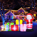 Santa inflatable ringing a bell beside a row of glowing gift boxes and a teddy bear at night