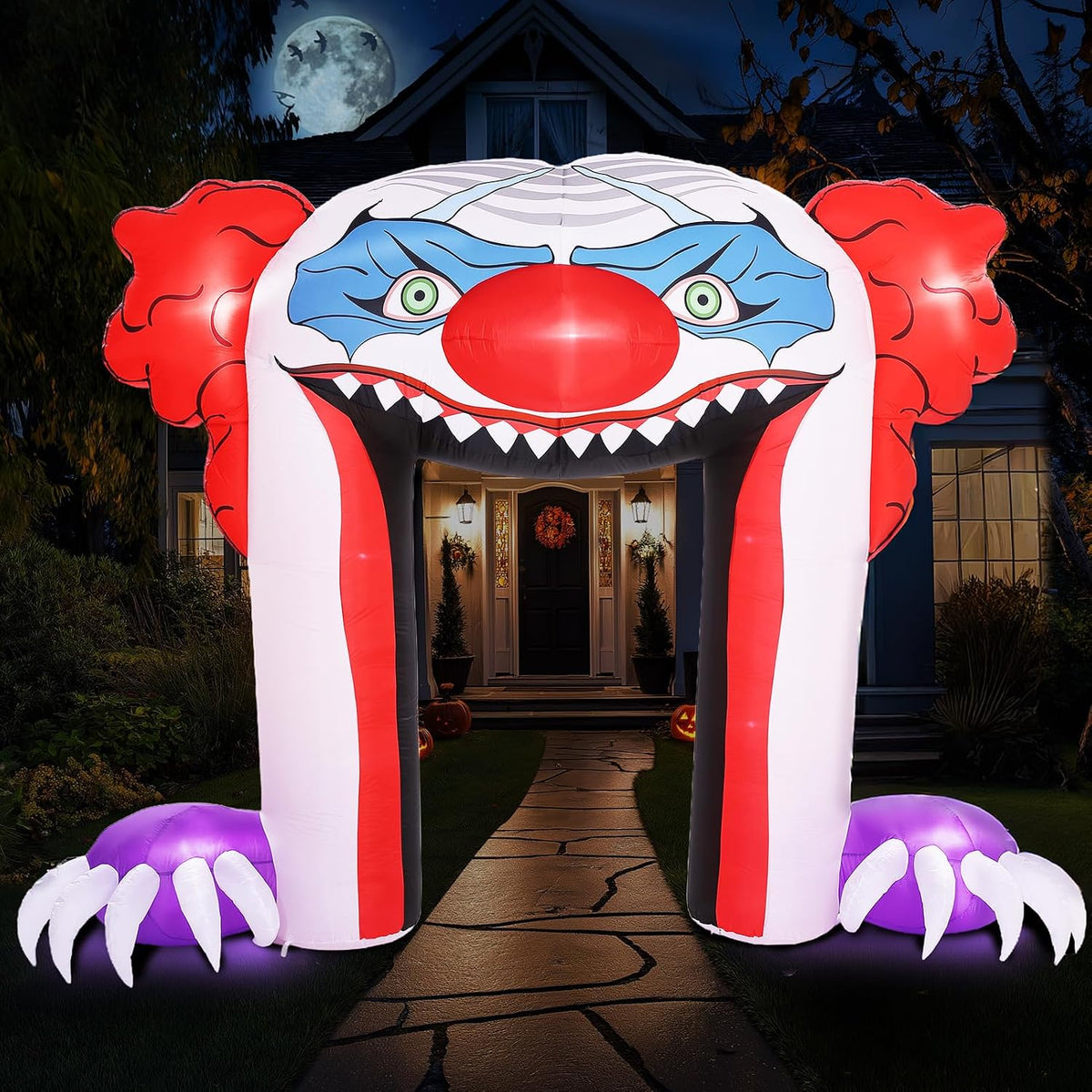 Giant creepy clown face archway inflatable with an open toothy mouth over a front walk at night