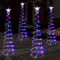 Four spiral Christmas trees with multicolor LEDs and star toppers glowing at night