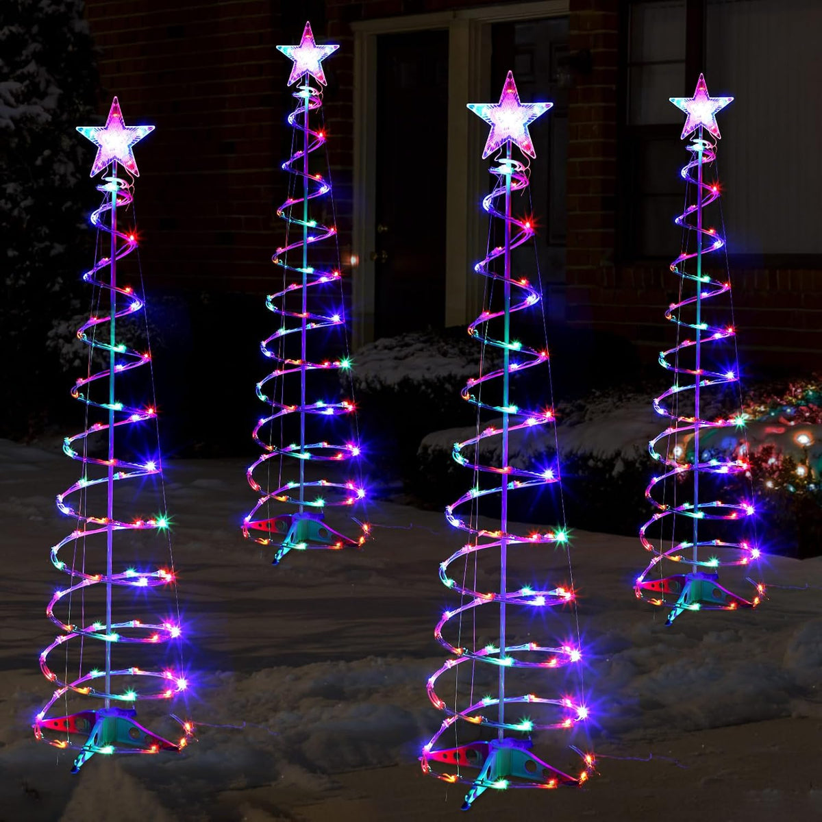 Four spiral Christmas trees with multicolor LEDs and star toppers glowing at night