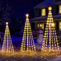 Three warm white LED cone Christmas trees of different heights with stars on a lawn at night